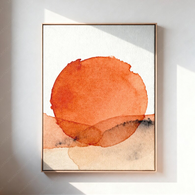 May include: A rectangular framed wall art piece featuring a large, vibrant orange watercolor circle centered against a white background. Below the circle, soft, translucent washes of light orange and muted gray paint create a layered horizon.