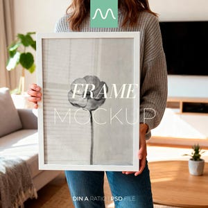 Puede incluir: Una maqueta de impresión artística enmarcada en blanco sostenida por una persona. La impresión presenta un diseño floral en blanco y negro con el texto "FRAME MOCKUP". El marco es rectangular y la imagen está en un entorno interior moderno.