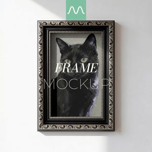 Op de afbeelding: Rechthoekige zwarte lijst met sierlijke zilveren details, met een portret van een zwarte kat met groene ogen. De woorden "FRAME MOCKUP" staan in het wit. De lijst hangt aan een witte muur.
