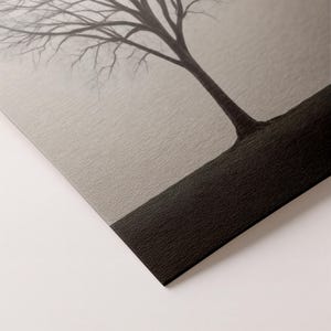 May include: A black and white art print featuring a bare tree against a misty, light gray background. The tree's trunk and branches are dark, contrasting with the softer tones of the sky. The print has a textured surface.