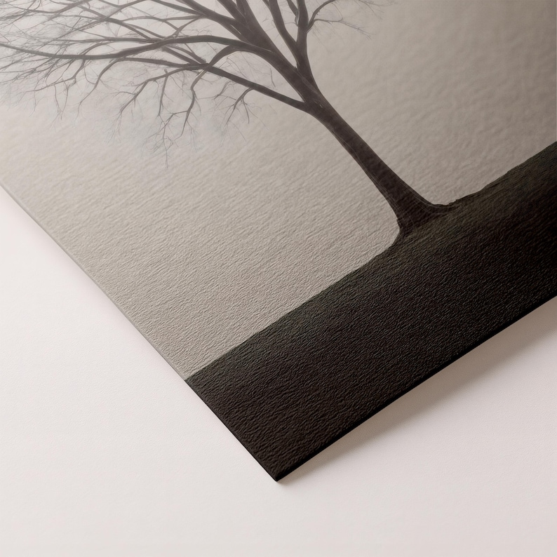 May include: A black and white art print featuring a bare tree against a misty, light gray background. The tree's trunk and branches are dark, contrasting with the softer tones of the sky. The print has a textured surface.