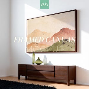 Puede incluir: Un lienzo enmarcado rectangular con una pintura de paisaje de montañas en tonos beige, terracota y verde. El texto FRAMED CANVAS MOCKUP está superpuesto. Debajo, una consola de madera oscura sostiene dos jarrones de vidrio de color verde.