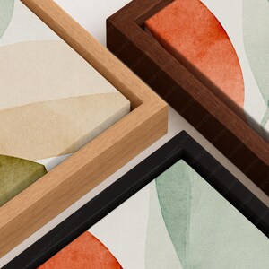 May include: Three rectangular canvas prints in floating frames. One frame is light wood, one is dark brown wood, and one is black. The canvases feature abstract shapes in muted tones of sage green, cream, and burnt orange with a textured finish.
