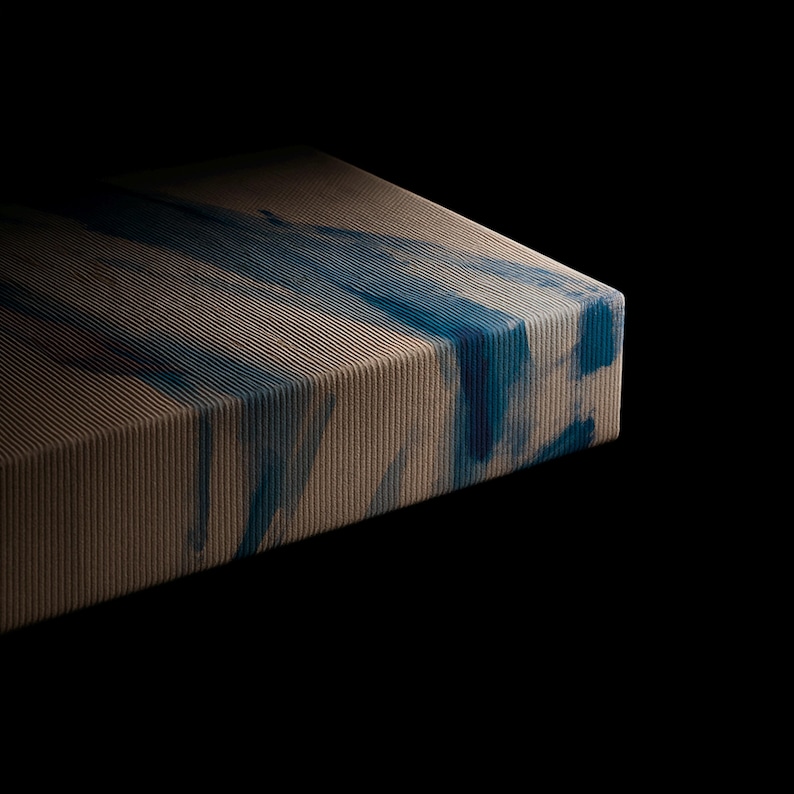 Puede incluir: Un panel de lienzo rectangular con una textura fina de acanalado vertical. La superficie muestra un degradado en tonos beige y arena, superpuesto con trazos abstractos y fluidos de pintura azul intenso que siguen las l&iacute;neas verticales.