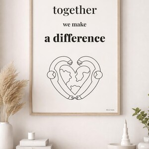 Könnte beinhalten: Ein gerahmter Druck mit den Worten "together we make a difference" in schwarzer Schrift. Darunter eine Schwarz-Weiß-Illustration von zwei Figuren, die eine herzförmige Weltkarte umarmen.