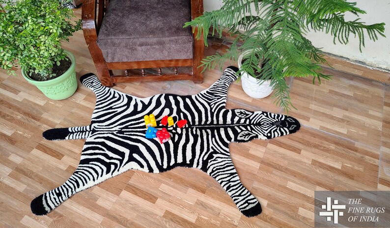 May include: A black and white zebra-patterned rug with a zipper down the middle. The rug is shaped like a zebra with legs and a head. Colorful toy blocks are placed on the rug. The rug is on a wooden floor.