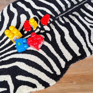 May include: A zebra-striped rug with a black and white pattern. Several colorful toy blocks in red, yellow, and blue are scattered on the rug. The rug is on a wooden floor.
