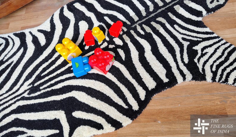 May include: A zebra-striped rug with a black and white pattern. Several colorful toy blocks in red, yellow, and blue are scattered on the rug. The rug is on a wooden floor.