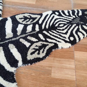 May include: A black and white zebra-striped rug with a leaf-shaped design. The rug has a soft, textured surface and is placed on a wooden floor. The rug's design includes a zebra pattern and leaf accents.