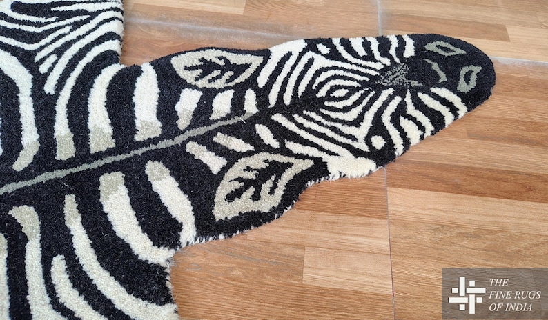 May include: A black and white zebra-striped rug with a leaf-shaped design. The rug has a soft, textured surface and is placed on a wooden floor. The rug's design includes a zebra pattern and leaf accents.