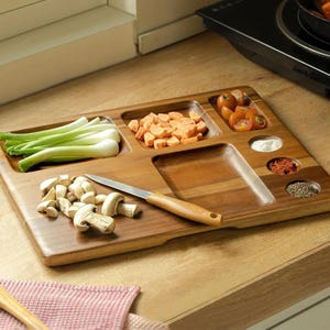 May include: A wooden cutting board with multiple compartments, filled with fresh ingredients. The board holds green onions, diced carrots, cherry tomatoes, mushrooms, and spices. A small knife rests on the board, ready for use. The board is made of a warm-toned wood.