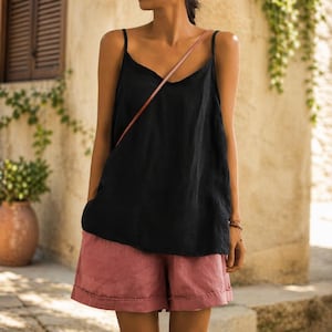 May include: A black camisole top with thin straps and a V-neck paired with pink shorts. The shorts have a rolled hem. The outfit is casual and suitable for warm weather.