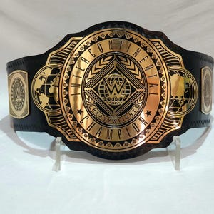 May include: A black and gold Intercontinental Heavyweight Championship belt. The belt features a large central plate with the WWE logo and the words "Intercontinental Heavyweight Champion". The side plates have the WWE logo and a globe design.