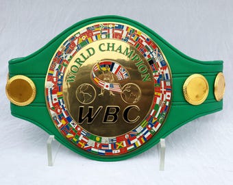 May include: A green and gold World Boxing Council (WBC) championship belt. The central plate displays "WORLD CHAMPION" and a boxer graphic. The belt is decorated with flags of many countries.
