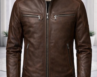 May include: A dark brown leather jacket featuring a stand-up collar with a snap button closure, a central metal zip, two horizontal zipped chest pockets, and two lower zipped pockets, displayed on a mannequin torso.
