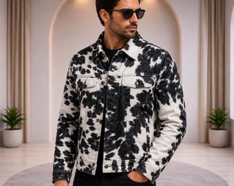 May include: A denim jacket featuring a black and white cow print pattern, a classic collar, long sleeves with buttoned cuffs, two chest pockets with flaps, and a front button closure. The jacket is worn over a plain black shirt.