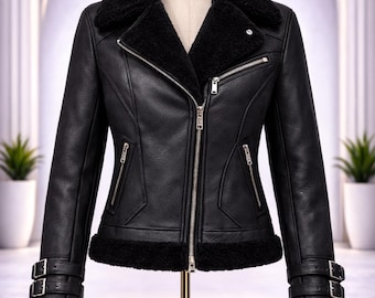 May include: A black leather-look jacket featuring a thick black faux-shearling collar, hem, and cuffs. The jacket includes a silver-toned front zipper, two zippered side pockets, one zippered chest pocket, and two adjustable buckled straps at each wrist.