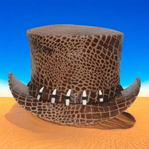 Puede incluir: Un sombrero de copa marrón con un patrón texturizado similar al de un reptil. El sombrero tiene un ala ancha y una banda adornada con detalles blancos y negros. El sombrero está sobre un paisaje desértico con cielo azul.