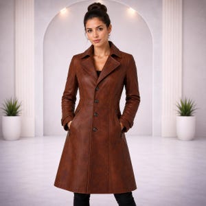 May include: A knee-length, brown leather coat featuring a notched lapel collar, long sleeves with cuff details, and a front button closure. The coat has a tailored fit with vertical seam detailing and two side pockets, providing a structured silhouette.