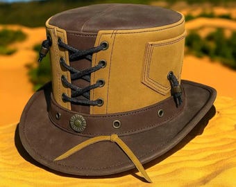 May include: A brown and tan leather top hat with a wide brim. The hat features a laced front, a decorative band, and a small pocket. A yellow leather strap hangs from the brim. The hat is designed for outdoor wear.