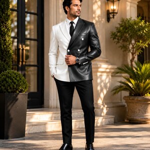 May include: A double-breasted blazer featuring a split design with a white right side and a black leather-look left side, paired with a black tie, black trousers, and black dress shoes. The blazer has white buttons and a structured lapel.