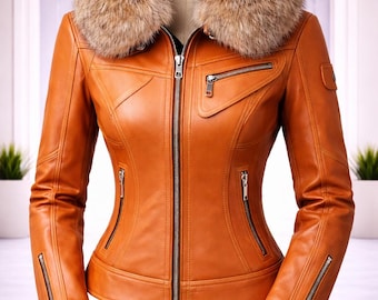 Könnte beinhalten: Eine hellbraune Lederjacke mit einem großen, flauschigen braunen Kunstfellkragen, einem durchgehenden silbernen Frontreißverschluss, zwei Reißverschlusstaschen an der Taille, einer Brusttasche und silbernen Reißverschlüssen an den Ärmelbündchen.
