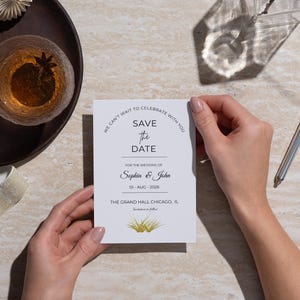 Elegant wedding save the date invitation card mockup held in hands on a luxury marble table, featuring minimalist wedding stationery design, decorative ribbon, glass accents, and modern wedding announcement details.