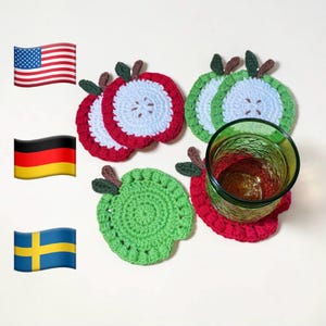 May include: Crocheted apple-shaped coasters in red, green, and white. The coasters have a detailed design, with a stem and leaf. A green glass sits on one of the coasters. The coasters are approximately 4 inches in diameter.