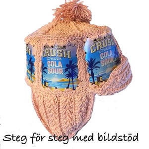 May include: A light pink crocheted hat with a pom-pom, displaying "CRUSH COLA SOUR" on the sides. The hat is crafted from soft yarn with a textured pattern. The text "PDF mönster på svenska" and "Steg för steg med bildstöd" are also visible.