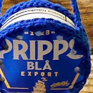 Könnte beinhalten: Ein blau-weißer Behälter mit dem Wort "PRIPP" in großen weißen Buchstaben. Der Behälter ist mit einem blauen Häkelmaterial umwickelt. Die Worte "BLA EXPORT" sind ebenfalls auf dem Behälter zu sehen.