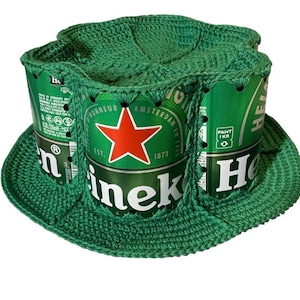 Może przedstawiać: Zielony kapelusz szydełkowy z puszkami piwa Heineken. Kapelusz ma szerokie rondo i zaokrągloną koronę, a puszki po piwie tworzą boki. Puszki Heineken są zielone z czerwoną gwiazdą.