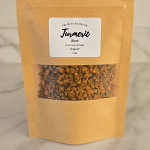 May include: A kraft paper bag with a clear window, filled with dried turmeric root. The bag has a white label with the text "Turmeric" and other details. The product is organic and weighs 1 oz.
