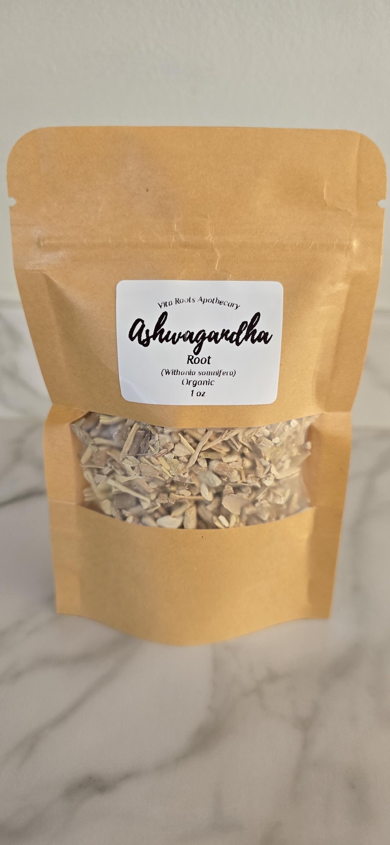 May include: A brown paper bag with a clear window, filled with dried root pieces. A white label displays the text "Vitu Roots Apothecary Ashwagandha Root (Withania somnifera) Organic 1 oz."