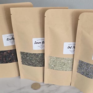 May include: Five stand-up kraft paper pouches with clear windows containing dried herbs and flowers labeled Calendula, Rosehips, Lemon Balm, Oat Tops, and Lavender. Each pouch displays a white label with black text and a weight of 1 oz.
