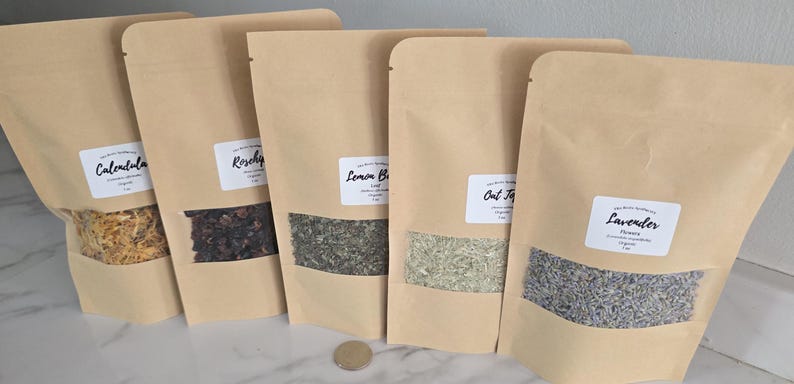 May include: Five stand-up kraft paper pouches with clear windows containing dried herbs and flowers labeled Calendula, Rosehips, Lemon Balm, Oat Tops, and Lavender. Each pouch displays a white label with black text and a weight of 1 oz.
