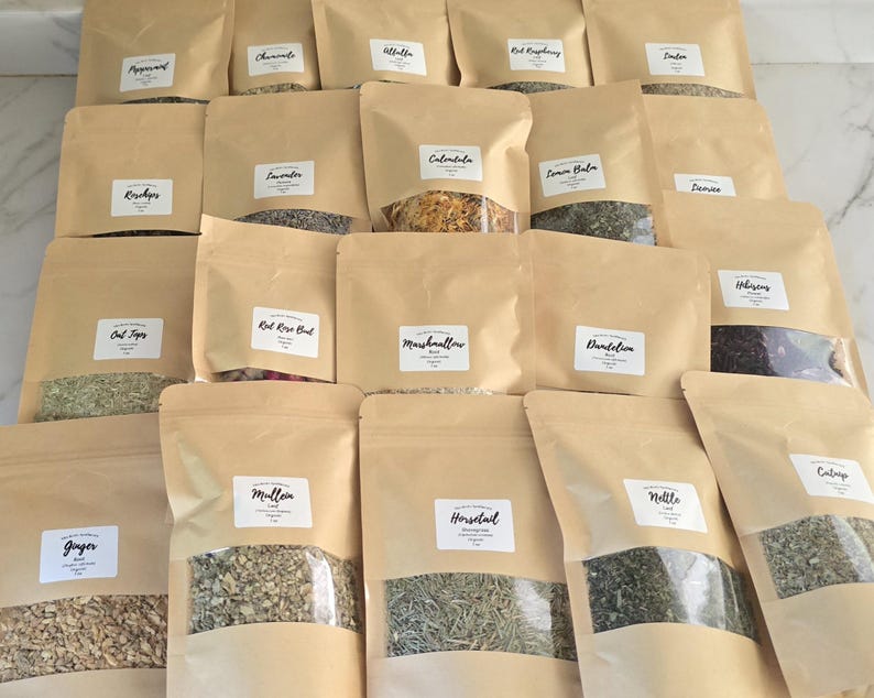 May include: A collection of twenty brown paper pouches containing various dried herbs and botanicals. Each pouch features a clear window at the bottom to display the contents and a white label with the name of the herb, including Peppermint, Chamomile, Alfalfa, Red Raspberry, Linden, Rosehips, Lavender, Calendula, Lemon Balm, Damiana, Oat Tops, Red Rose Bud, Marshmallow, Dandelion, Hibiscus, Ginger, Mullein, Horsetail, Nettle, and Catnip.