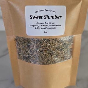 May include: A brown paper bag with a clear window, filled with dried herbs. A white label reads "Sweet Slumber" and lists the organic tea blend ingredients: Mugwort, Lavender, Lemon Balm, and German Chamomile. The bag contains 1 oz.