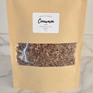 May include: A brown paper bag with a clear window displaying cinnamon sticks. The bag has a white label with the text "Cinnamon Ceylon (Cinnamomum verum) Organic 1 oz" and the brand name "Vito Roots Apothecary".