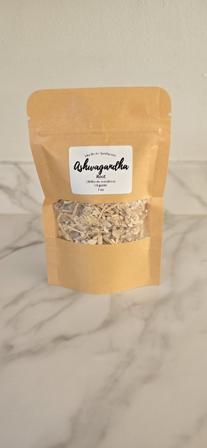 May include: A brown paper bag with a clear window, filled with dried ashwagandha root. The label reads "Ashwagandha Root" and includes the brand name "Vita Roots Apothecary", the botanical name, and the weight, 1 oz.