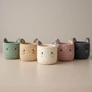 Puede incluir: Cinco cestas de ganchillo en colores pastel: verde menta, beige, crema, rosa y gris antracita. Cada cesta tiene forma de cara de gato, con orejas, ojos bordados y bigotes. Ideales para el almacenamiento.