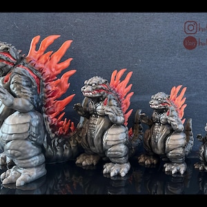May include: A set of four Godzilla figurines in varying sizes. The figures are primarily gray with red dorsal fins and accents. The largest figure is on the left, with the smallest on the right. The figures are posed in a standing position.