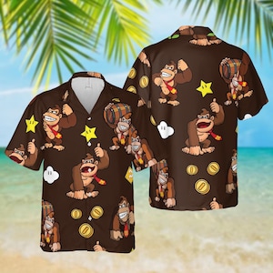 May include: Brown button-down shirt featuring a repeating pattern of a cartoon gorilla character with a red tie, stars, coins, and barrels. The short-sleeved shirt has a white collar and is set against a beach background.