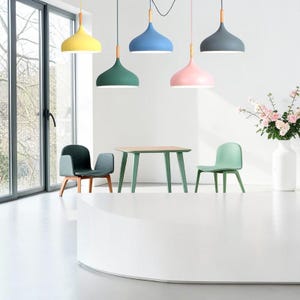 May include: A modern interior scene featuring five pendant lights in yellow, blue, green, pink, and gray. Each light has a wooden accent. A green table and chairs are in the foreground, with a white vase of flowers on the right.