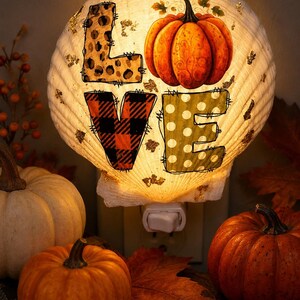 May include: A seashell night light featuring the word LOVE in block letters, with the L in leopard print, the O as an orange pumpkin, the V in red and black buffalo plaid, and the E in green with white polka dots, illuminated with gold accents.