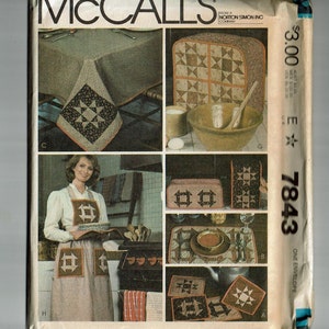 May include: A vintage McCall's sewing pattern envelope for a quilted kitchen set. The pattern includes instructions for making a table runner, placemats, potholders, and an appliance cover. The pattern is for size E 7843 and costs $3.00.