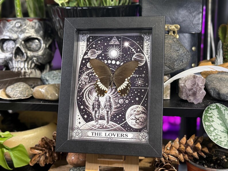 Puede incluir: Una impresi&oacute;n en blanco y negro enmarcada que presenta una mariposa y elementos c&oacute;smicos. La impresi&oacute;n incluye las palabras "THE LOVERS". La mariposa es marr&oacute;n con marcas blancas. El marco es negro.