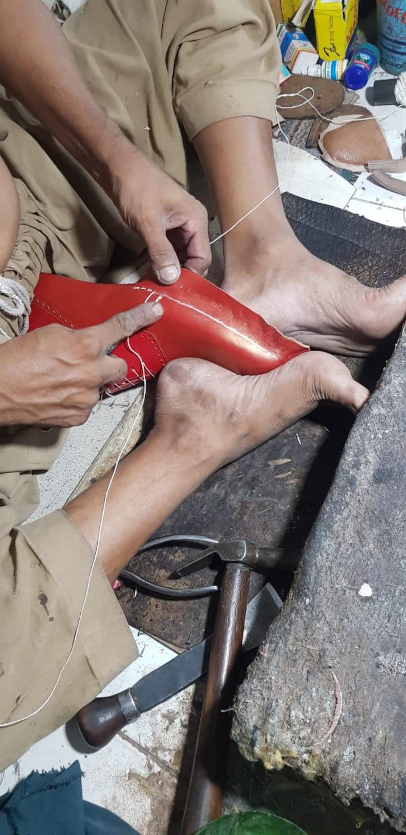 Pu&ograve; includere: Mani di un calzolaio che cuce una scarpa in pelle rossa. Il calzolaio usa ago e filo. Sono visibili strumenti come un martello e delle pinze.