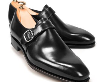 May include: A pair of black leather dress shoes with a single strap and buckle closure. The shoes have a polished finish and are displayed on a white background. The shoes are approximately 12 inches long.
