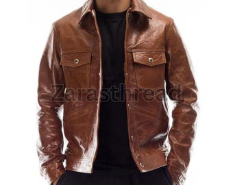 May include: A brown leather jacket with two chest pockets and button closures. The jacket has a collared neckline and is open, revealing a black shirt underneath. The text "Zarasththre" is visible on the jacket.