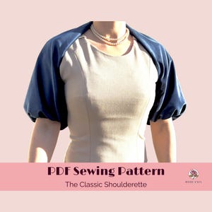 Pode incluir: Uma ombreira azul marinho com mangas curtas, usada sobre um vestido bege. A imagem inclui o texto "PDF Sewing Pattern" e "The Classic Shoulderette" em uma faixa rosa.